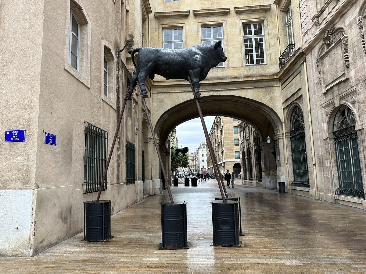 Bronze bull sculpture on metal stilts under a stone archway in Marseille near the Vieux-Port