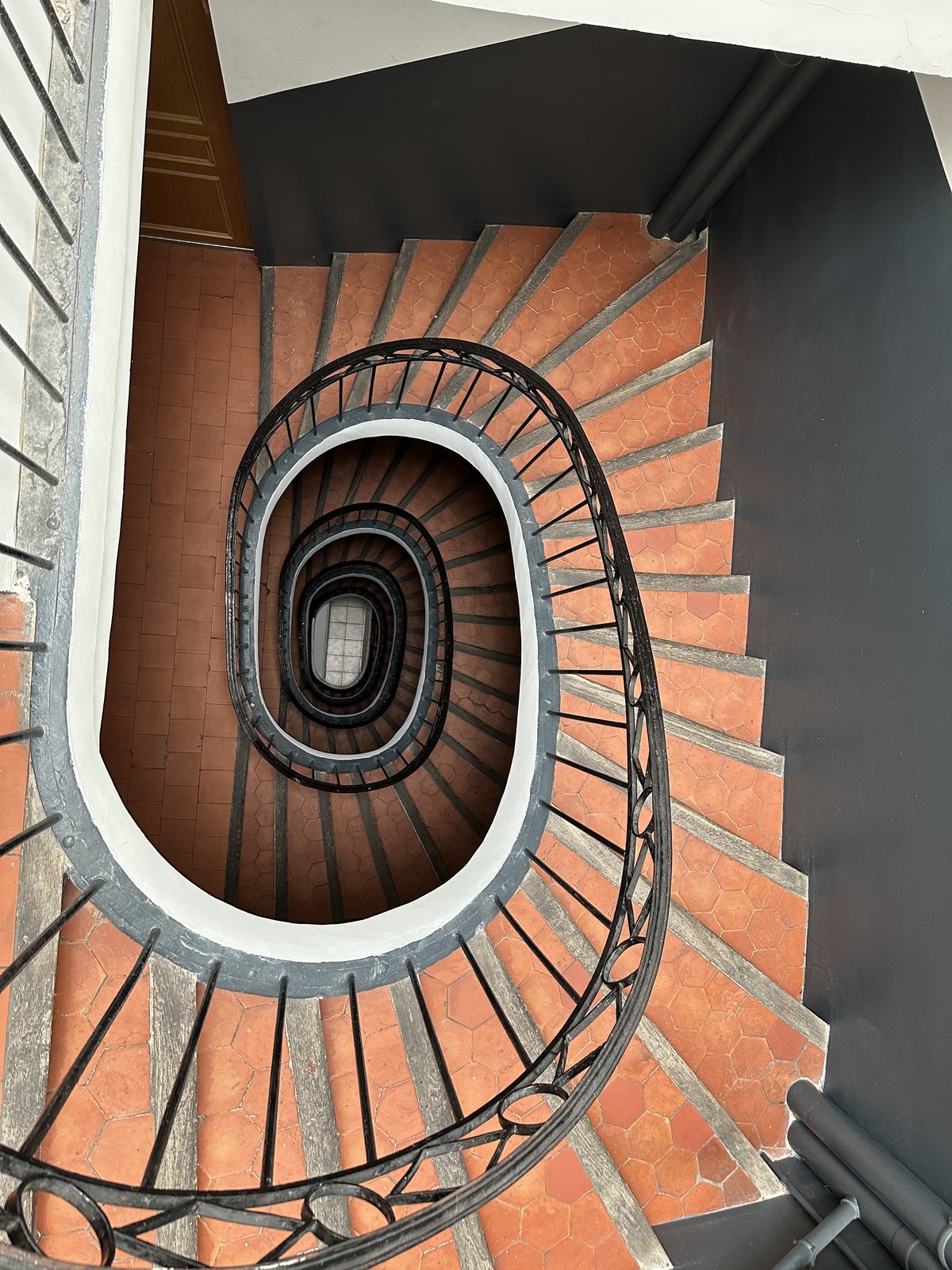 Spiral staircase viewed from above with terracotta hexagonal floor tiles and wrought iron railing in a Marseille building
