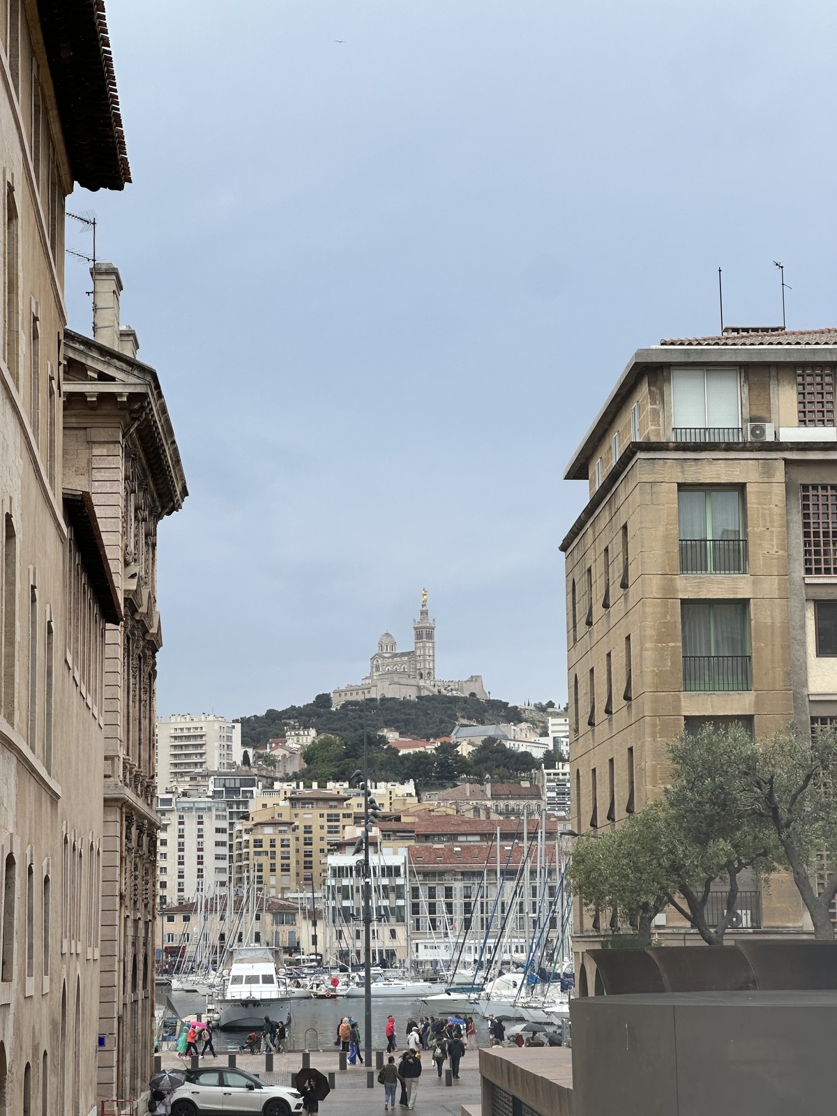 Street view toward the Vieux-Port in Marseille with Notre-Dame de la Garde basilica visible on the hilltop