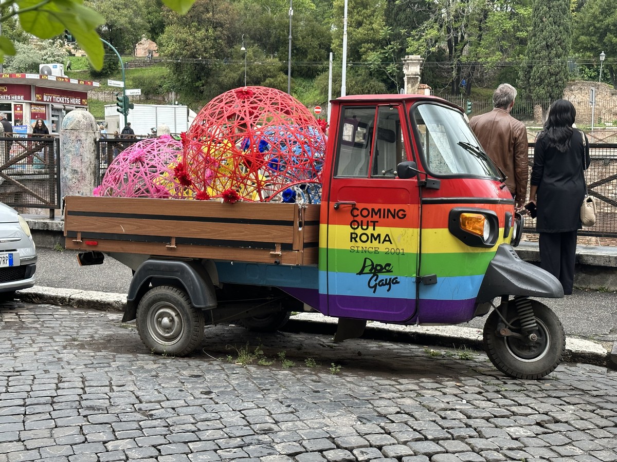 A small three-wheeled Ape truck painted in rainbow pride colors on a Rome street