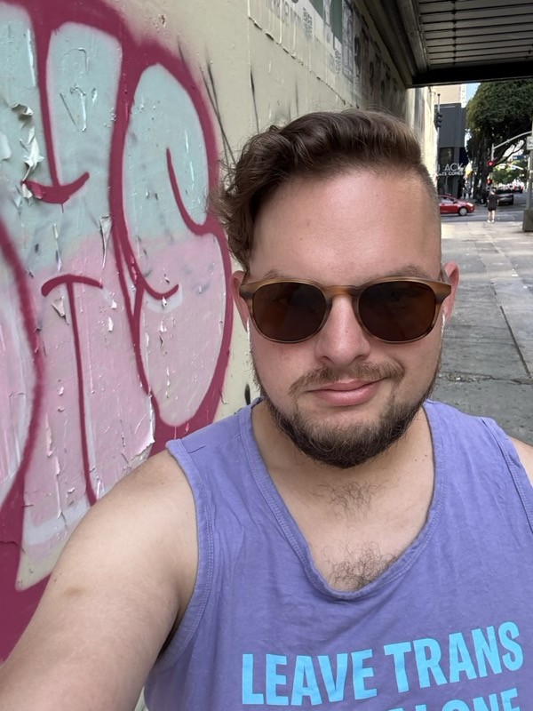 Selfie on a Los Angeles street with colorful street art, wearing a ‘Leave Trans Kids Alone’ purple tank top