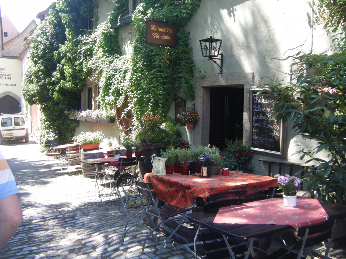 Vine-covered German Weinstube with outdoor tables on cobblestones