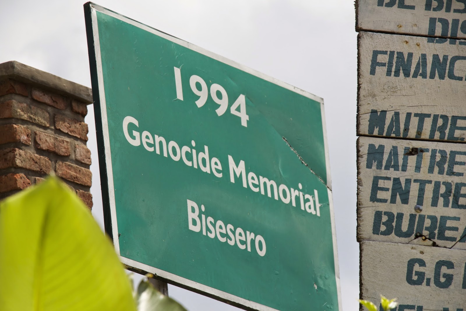Green entrance sign reading 1994 Genocide Memorial Bisesero mounted on a brick column