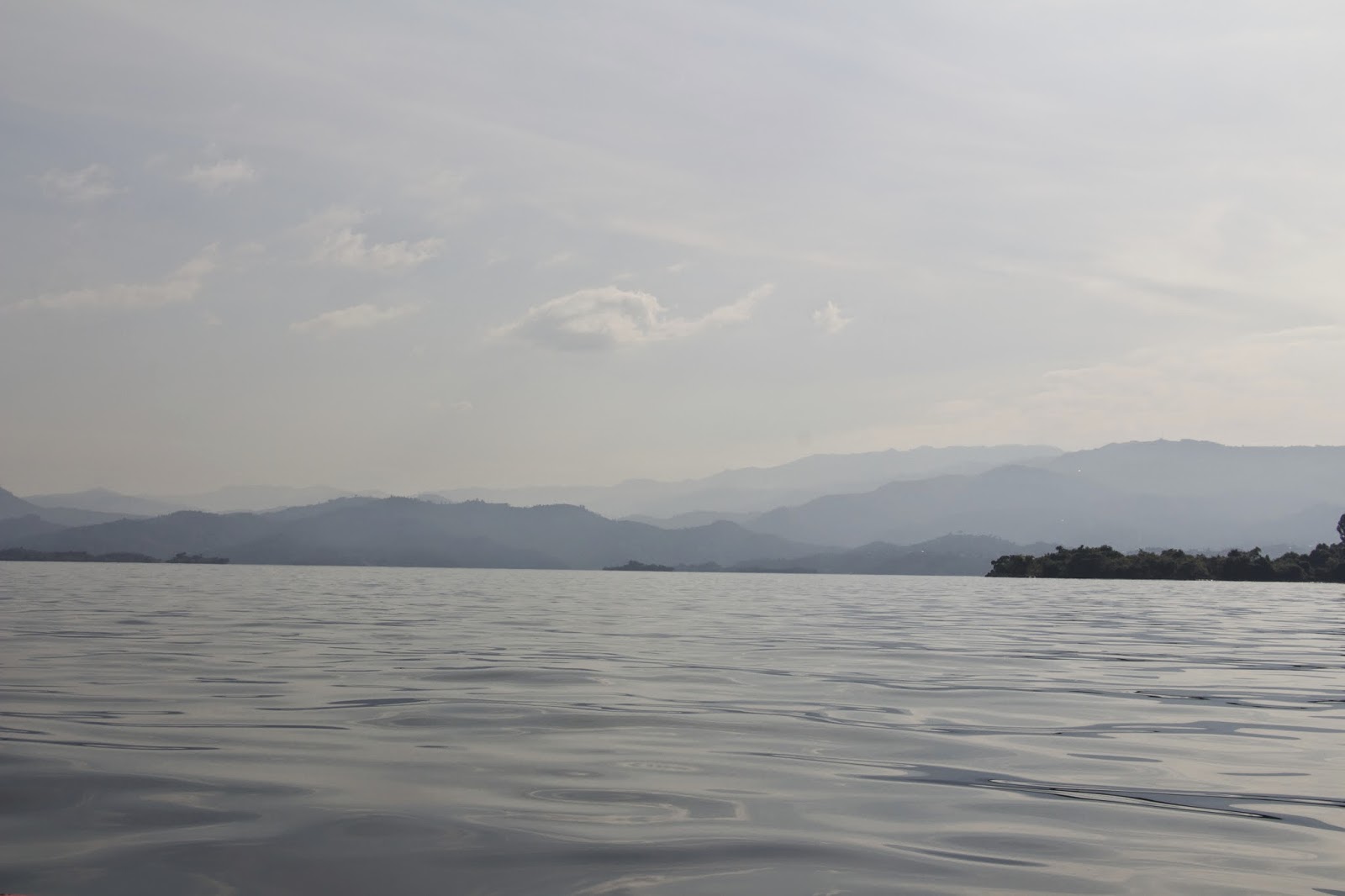 Wide view from a boat on Lake Kivu with misty mountains and hills in the distance