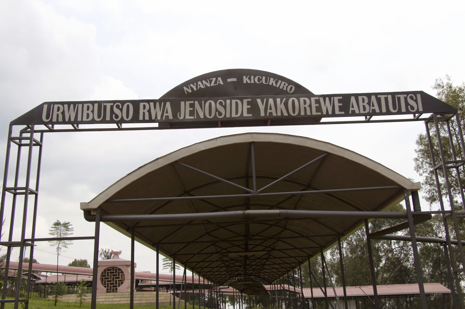 Entrance gate to the Nyanza-Kicukiro genocide memorial with sign reading Urwibutso Rwa Jenoside Yakorewe Abatutsi