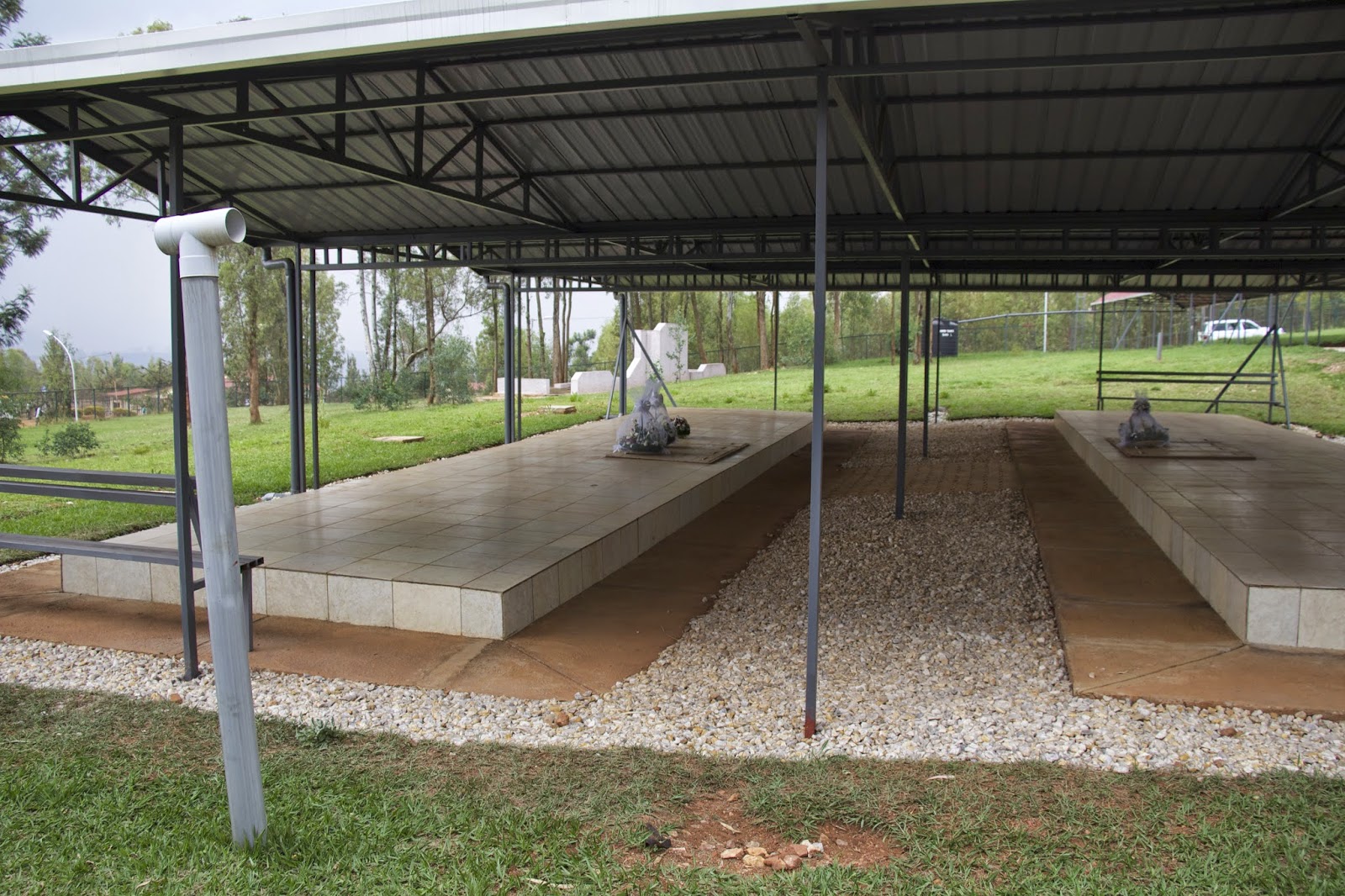 Covered mass graves with tiled platforms under a metal shelter at the Nyanza-Kicukiro memorial