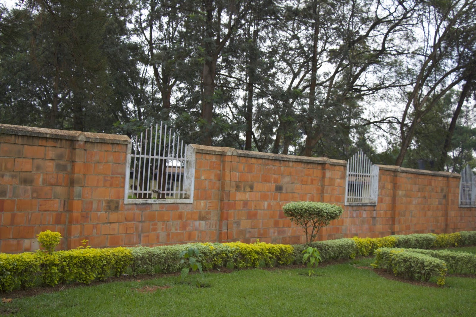 Brick perimeter wall with metal grate windows and landscaped hedges at the ETO school campus