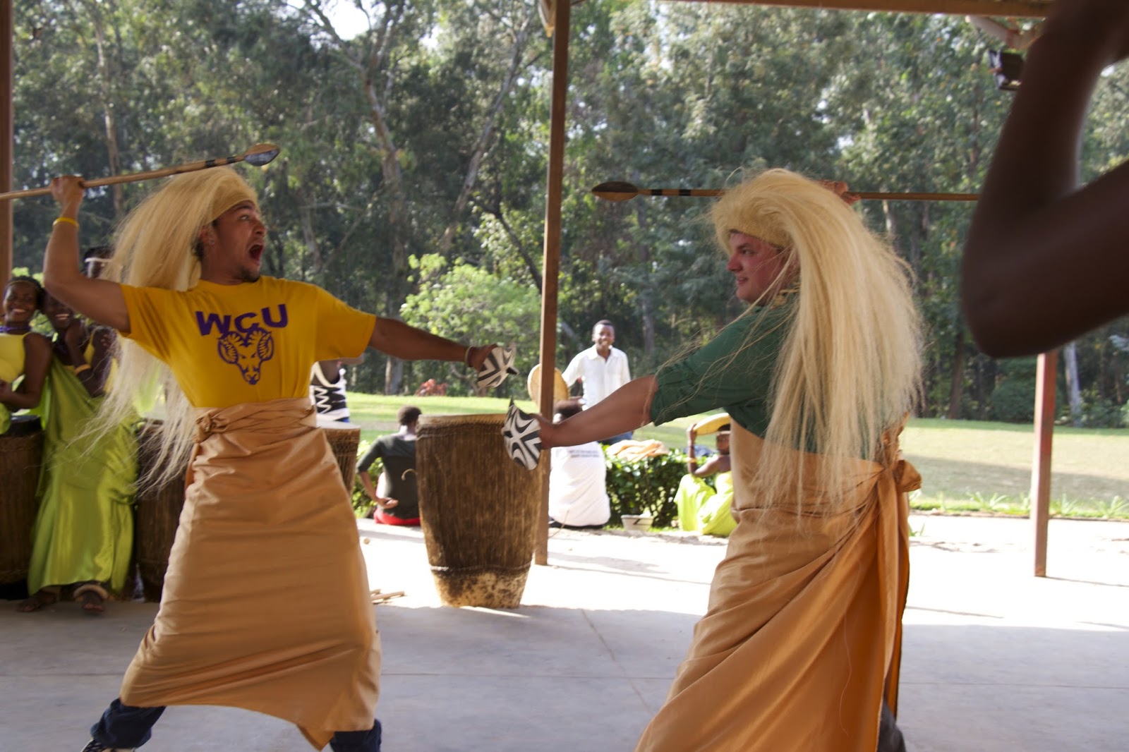 Two people from the group dressed in traditional Rwandan dance costumes performing under a pavilion