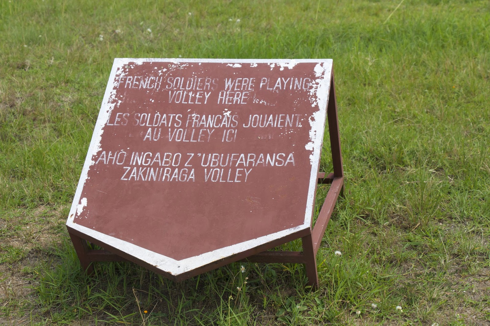 Sign reading 'French soldiers were playing volley here' in English, French, and Kinyarwanda, marking where a volleyball court was built on a mass grave