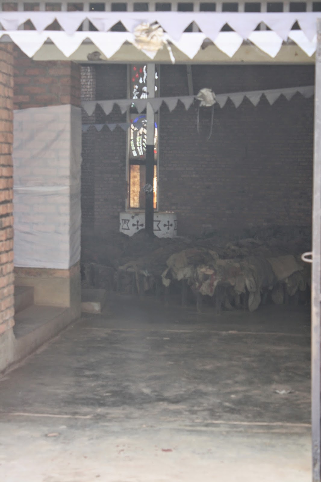 View through the church entrance into the dark interior where piles of victims' clothing are visible near the altar and stained glass window