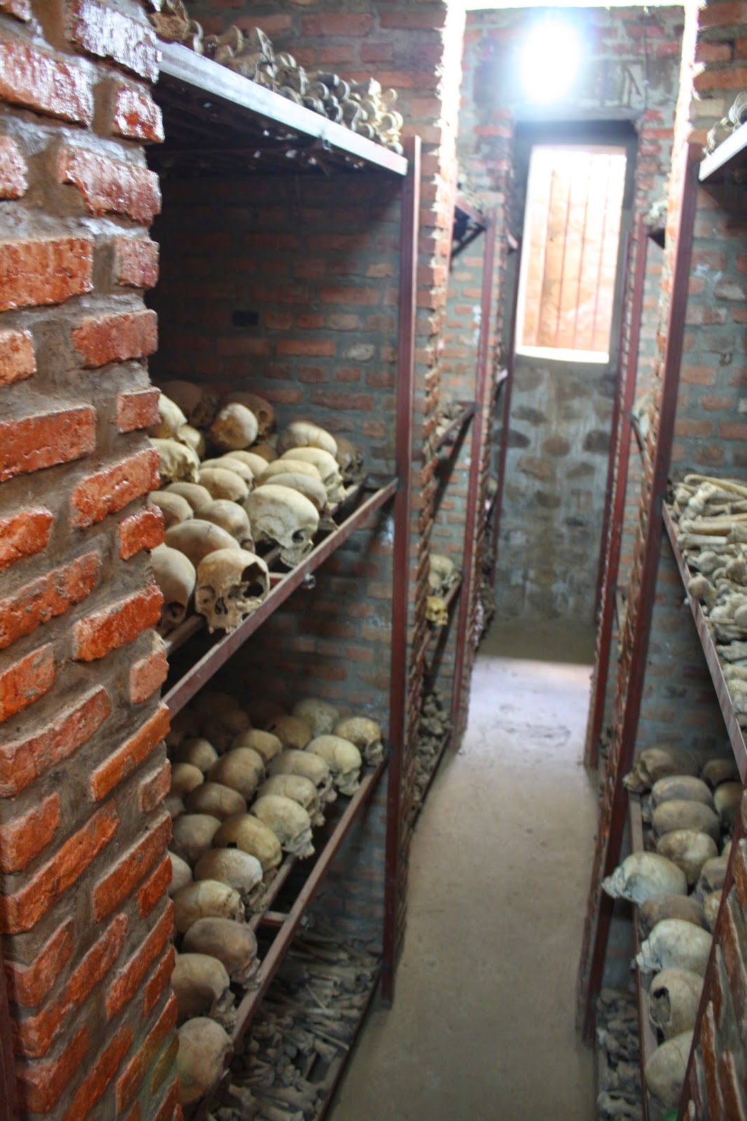 Narrow corridor between shelving units stacked floor to ceiling with skulls and bones in the underground mass grave at Nyamata Church