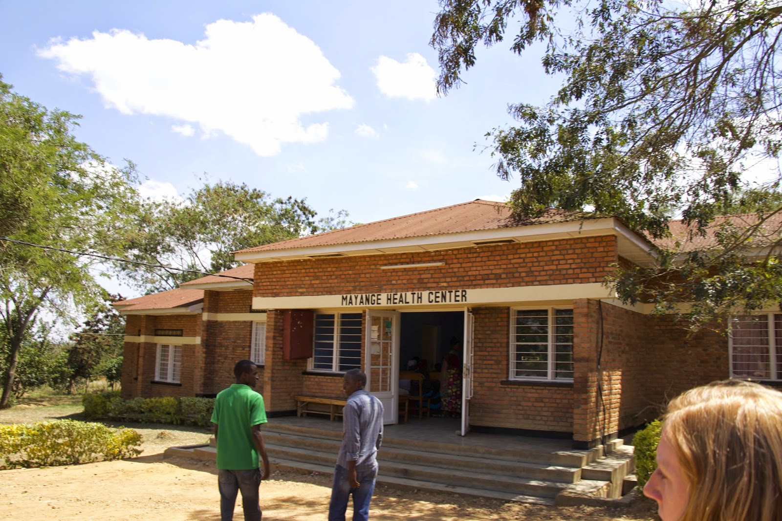 The Mayange Health Center building, a brick structure with people outside the entrance