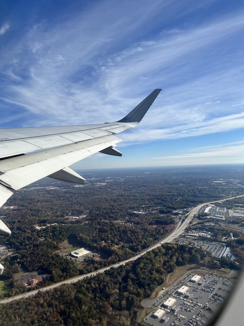 Aerial view from a plane window showing highway and suburban landscape during departure