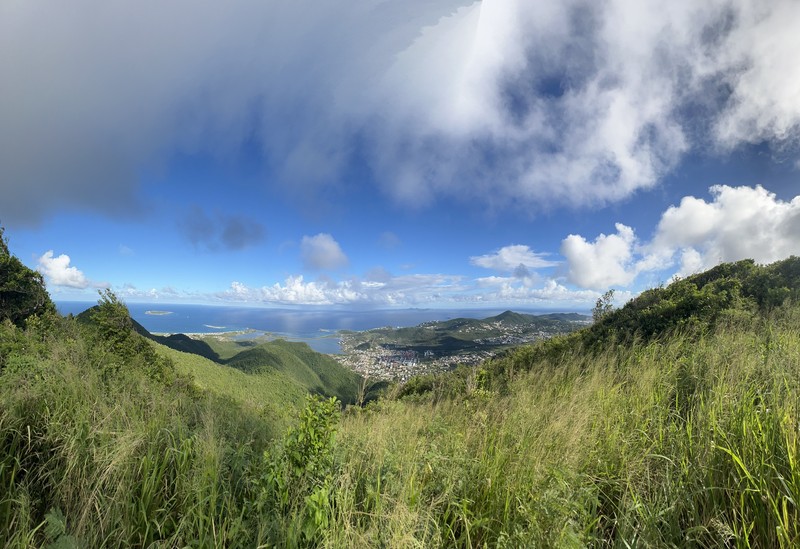 Wide panoramic view from grassy peak showing the full island under dramatic clouds