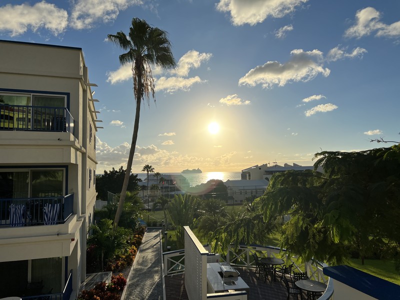 Resort building with palm tree silhouetted against the sun, cruise ship on the horizon