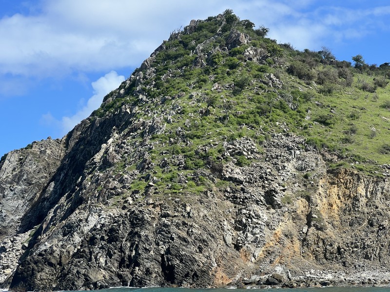 Tall rocky cliff with green vegetation seen from the water