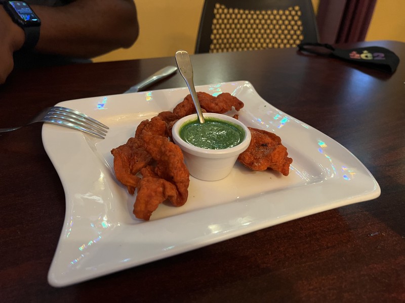 Fried fritters with green chutney sauce on a white plate