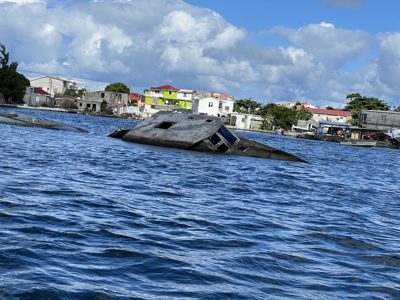 Sunken boat wreck in harbor with colorful houses on the hillside behind it