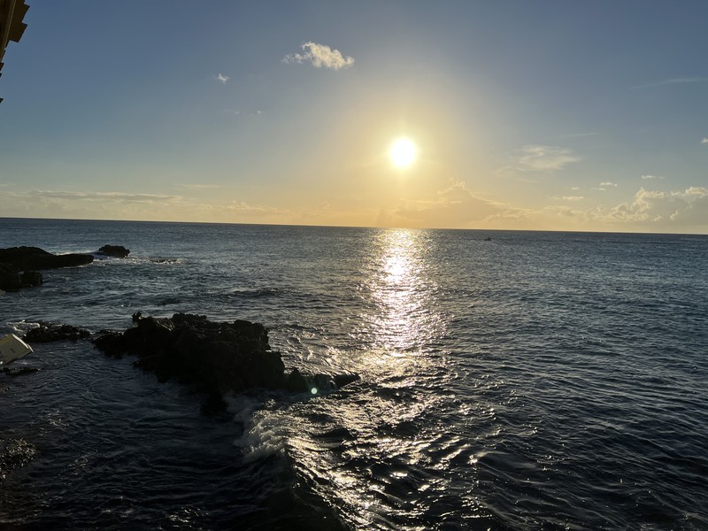 Sunset over rocky coastline with golden light, waves, and black volcanic rocks