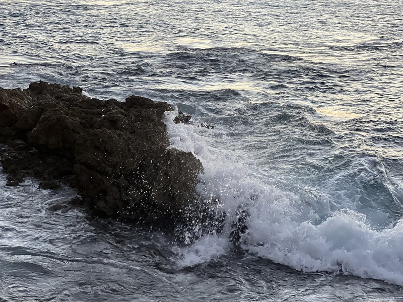 Waves crashing on dark volcanic rocks, moody close-up