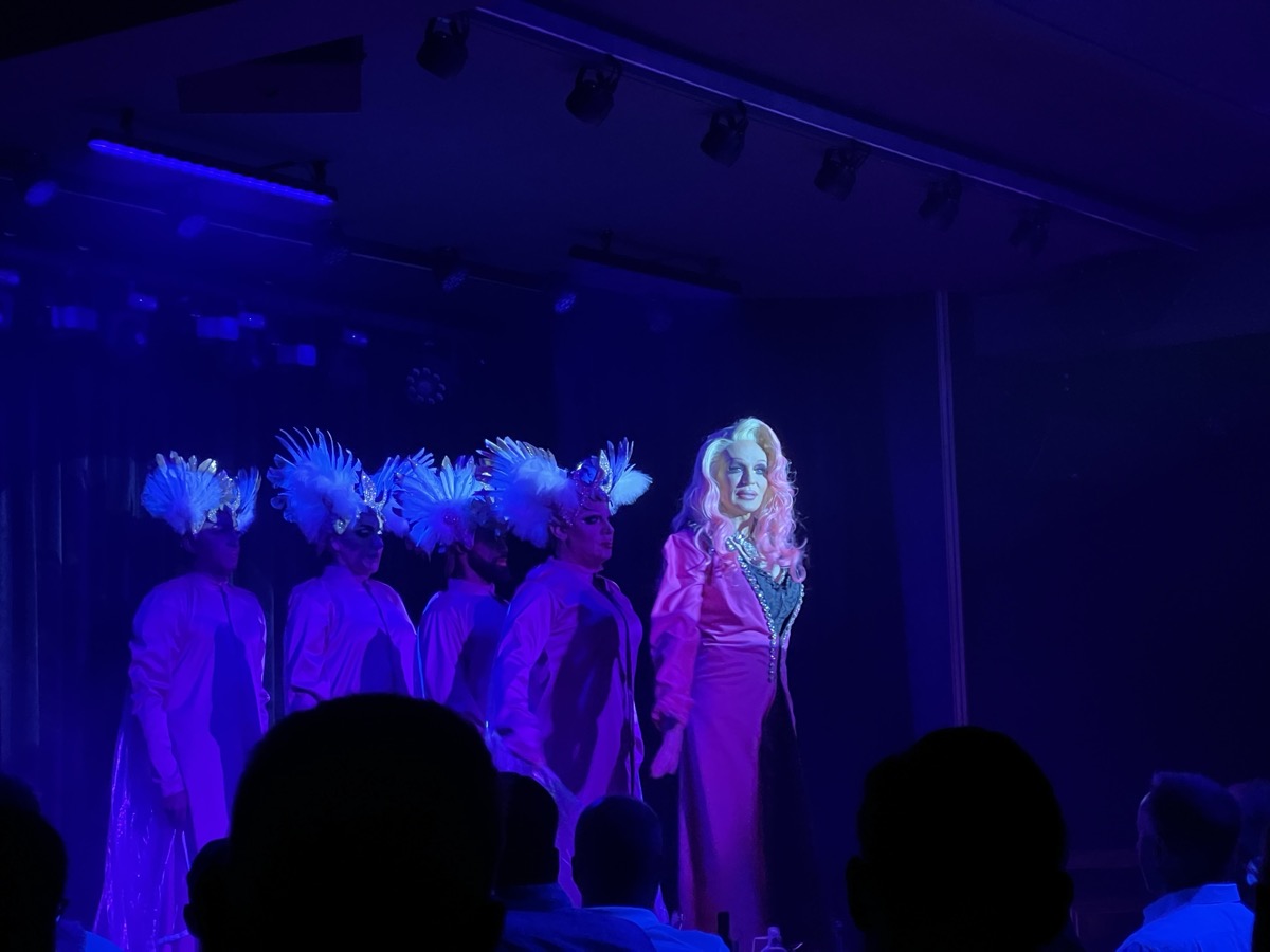 Cabaret performers in feathered headdresses with performer in pink satin gown
