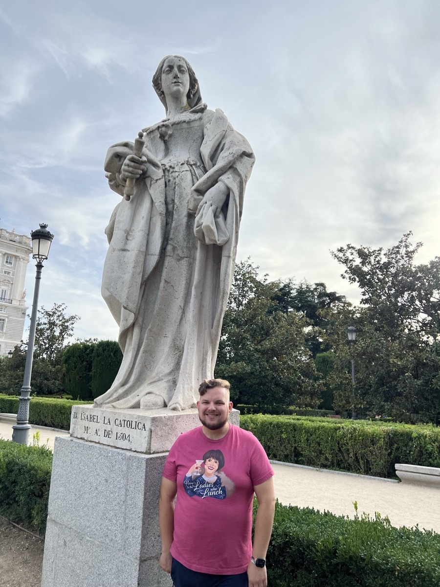 Michael posing with a stone statue of Isabel la Católica on a Madrid street