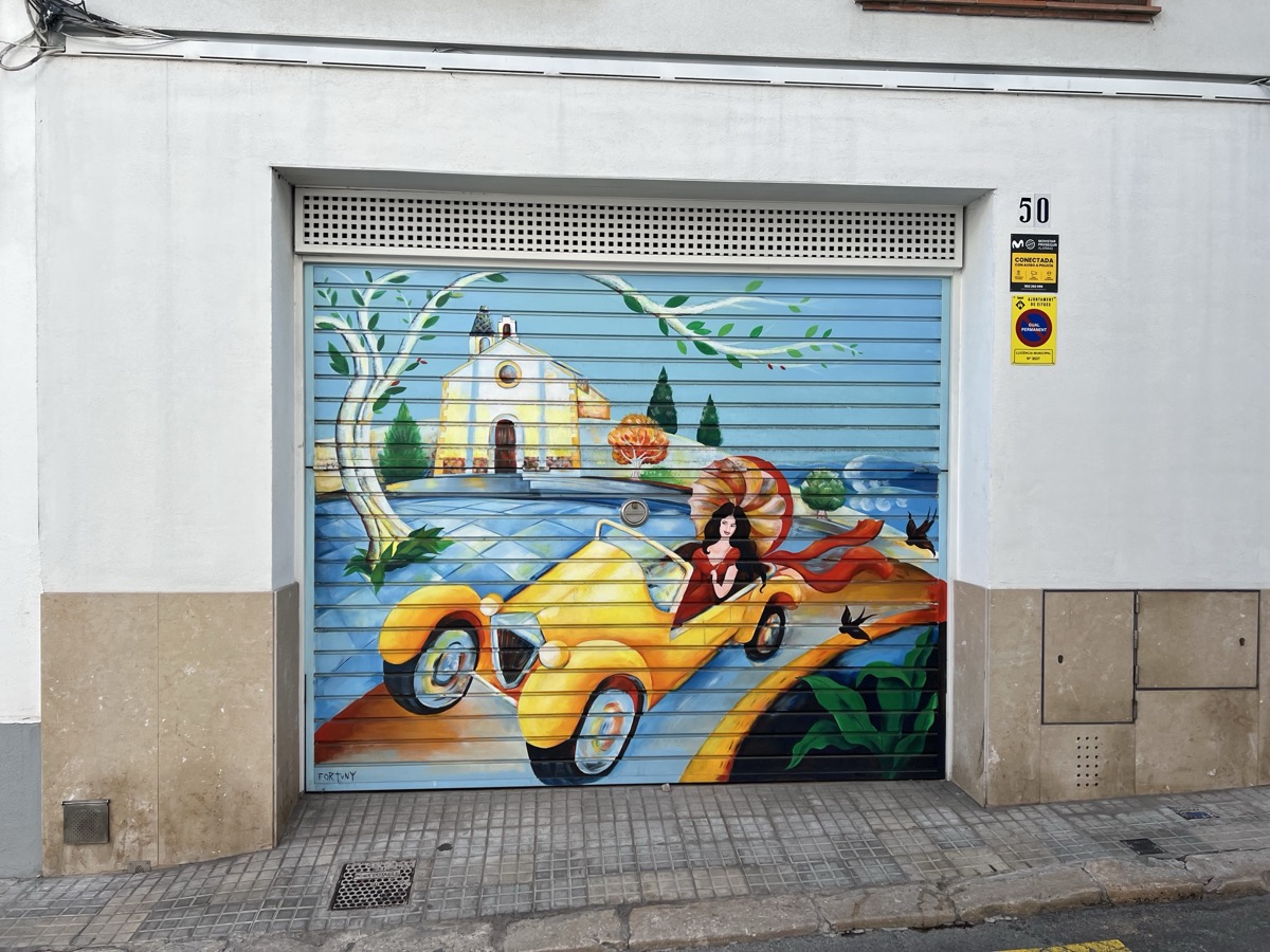 Colorful street art mural of a vintage car and church in Sitges